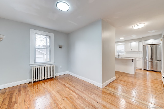 spare room featuring radiator, baseboards, plenty of natural light, and light wood finished floors