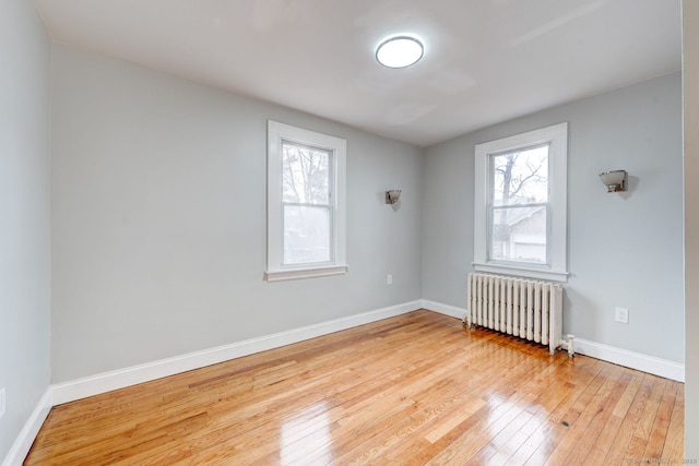 spare room with baseboards, radiator heating unit, and light wood-style floors