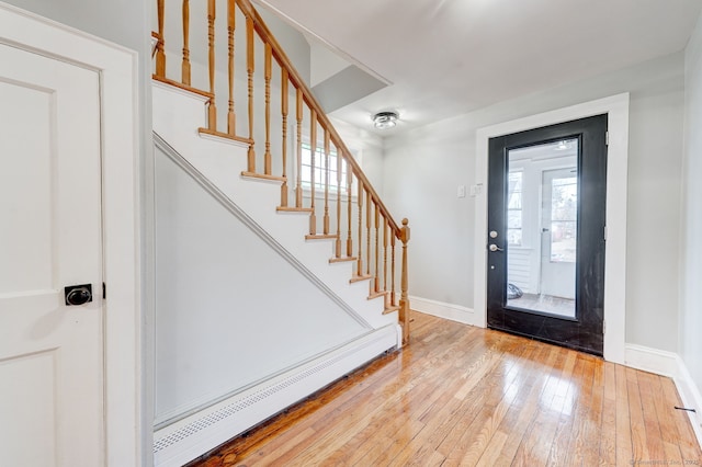 foyer with baseboards, wood-type flooring, baseboard heating, and stairs