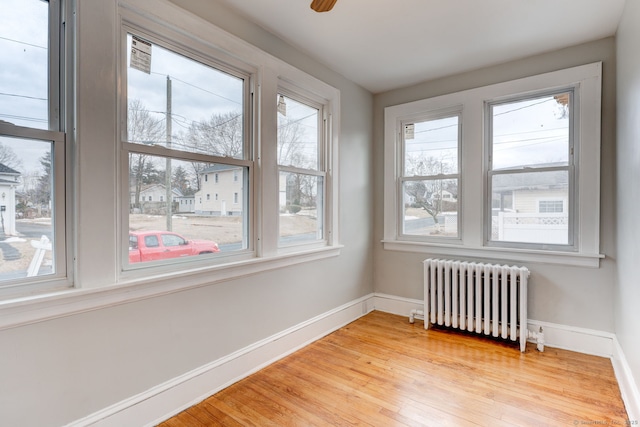 empty room featuring light wood finished floors, ceiling fan, radiator heating unit, and baseboards