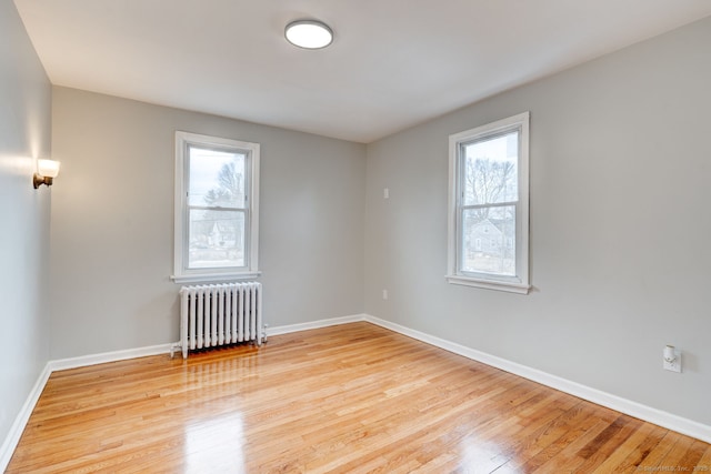 unfurnished room with radiator, a healthy amount of sunlight, light wood-type flooring, and baseboards