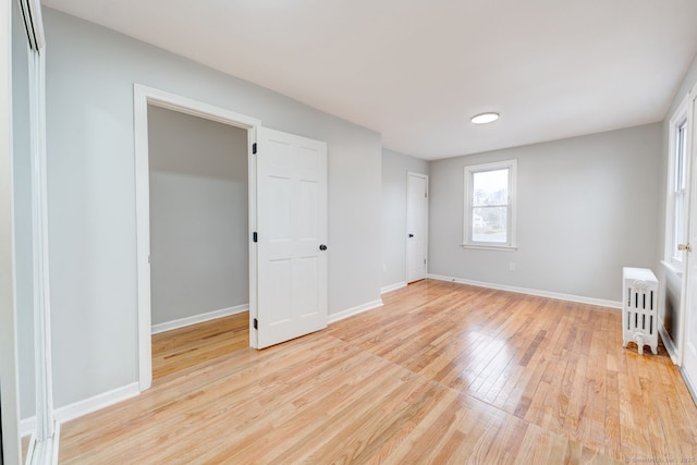 unfurnished bedroom with radiator, baseboards, and light wood-style floors