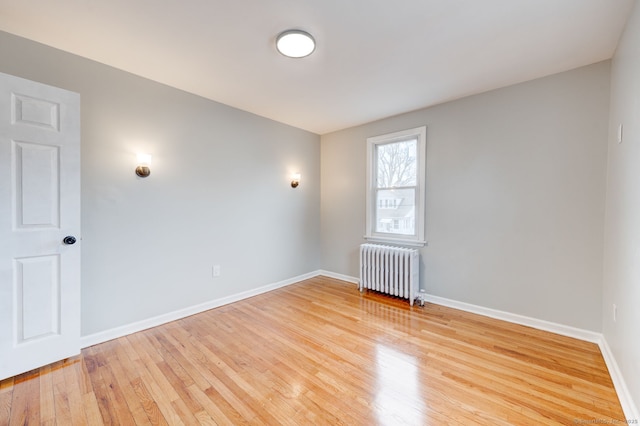 empty room featuring baseboards, radiator, and hardwood / wood-style flooring