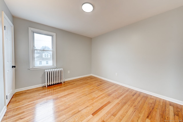 spare room featuring baseboards, radiator heating unit, and light wood finished floors