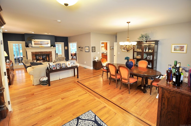 dining room featuring baseboards, wood finished floors, a brick fireplace, and a chandelier