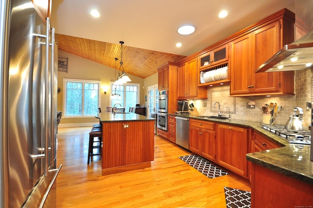 kitchen with a sink, appliances with stainless steel finishes, wall chimney range hood, decorative backsplash, and lofted ceiling