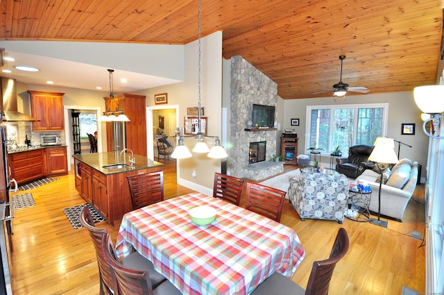 dining space with baseboards, wood ceiling, vaulted ceiling, a stone fireplace, and light wood-style flooring