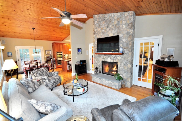 living room with light wood-type flooring, high vaulted ceiling, a ceiling fan, a stone fireplace, and wooden ceiling