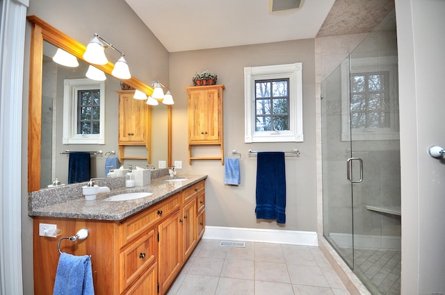 full bath with tile patterned flooring, baseboards, double vanity, a stall shower, and a sink