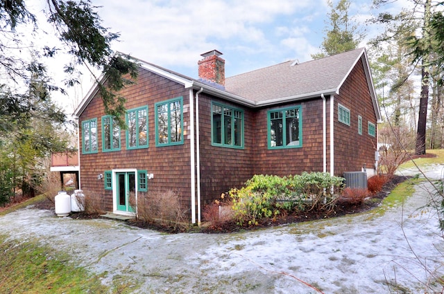 rear view of property with central AC, a chimney, and a shingled roof