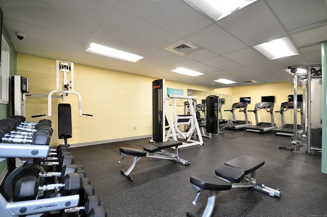 exercise room featuring visible vents, a paneled ceiling, and baseboards