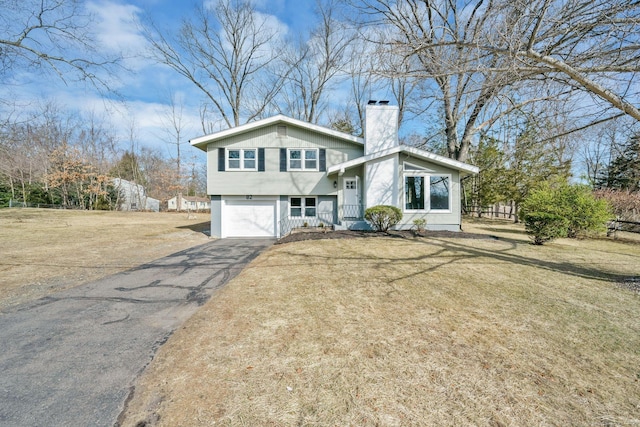 view of front facade featuring aphalt driveway, a garage, a front yard, and a chimney