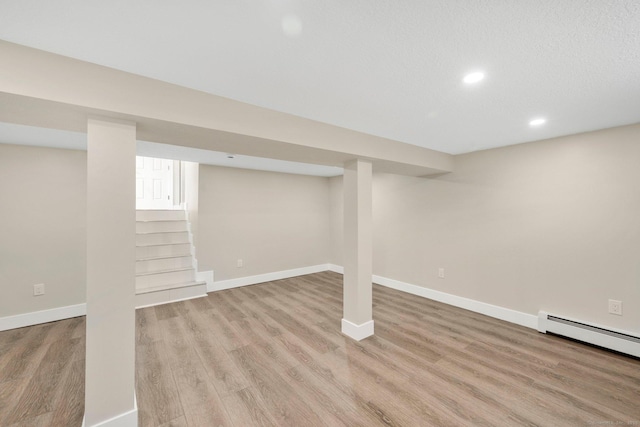 finished basement with a baseboard heating unit, recessed lighting, light wood-style floors, and baseboards