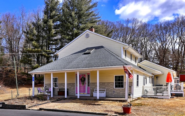 view of front facade featuring stone siding, roof with shingles, a porch, and a chimney