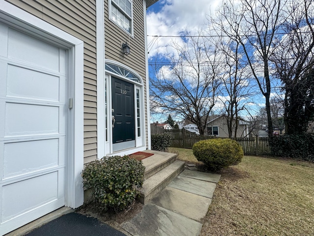 view of exterior entry featuring a garage, a lawn, and fence