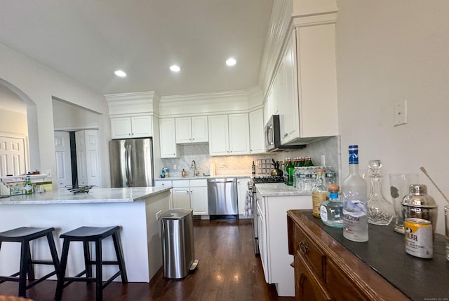 kitchen featuring arched walkways, decorative backsplash, appliances with stainless steel finishes, a kitchen breakfast bar, and a sink