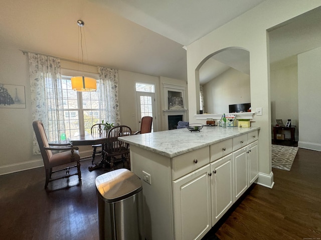 kitchen with baseboards, white cabinets, dark wood-type flooring, light stone countertops, and vaulted ceiling