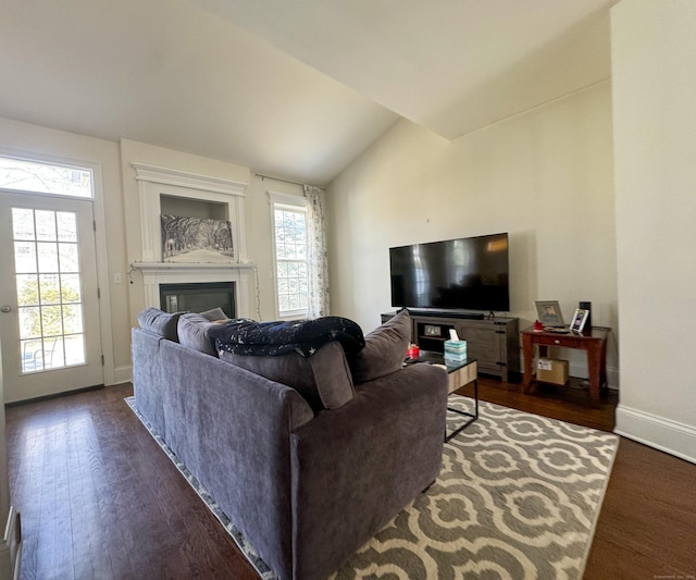 living room with dark wood-style floors, plenty of natural light, vaulted ceiling, and a glass covered fireplace