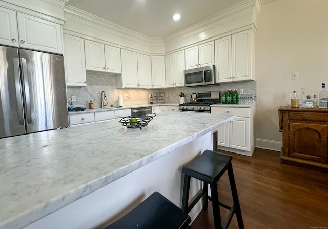 kitchen featuring dark wood finished floors, a breakfast bar area, decorative backsplash, appliances with stainless steel finishes, and white cabinetry