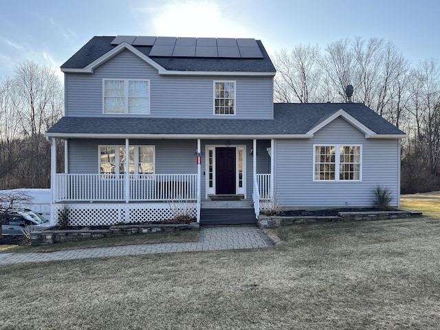 view of front of home featuring solar panels, a porch, a shingled roof, and a front yard