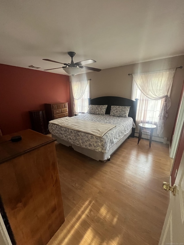 bedroom with multiple windows, light wood finished floors, and a baseboard radiator