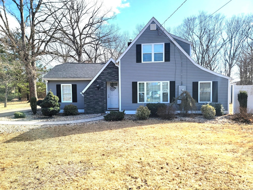 view of front of home with a front yard, fence, stone siding, and a chimney