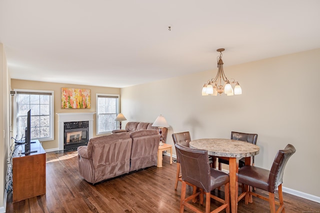 dining room featuring dark wood-style floors, a chandelier, baseboards, and a premium fireplace