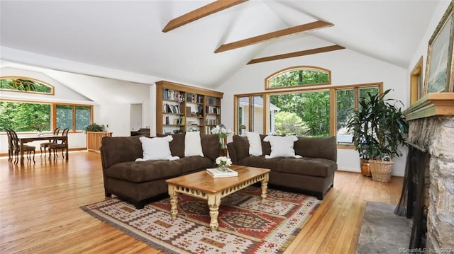 living area with wood finished floors, beamed ceiling, a fireplace with raised hearth, and high vaulted ceiling