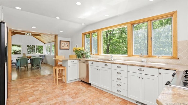 kitchen with light stone countertops, vaulted ceiling, stainless steel dishwasher, white cabinets, and a sink