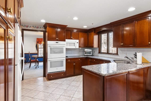 kitchen featuring a sink, light stone counters, white appliances, a peninsula, and light tile patterned floors