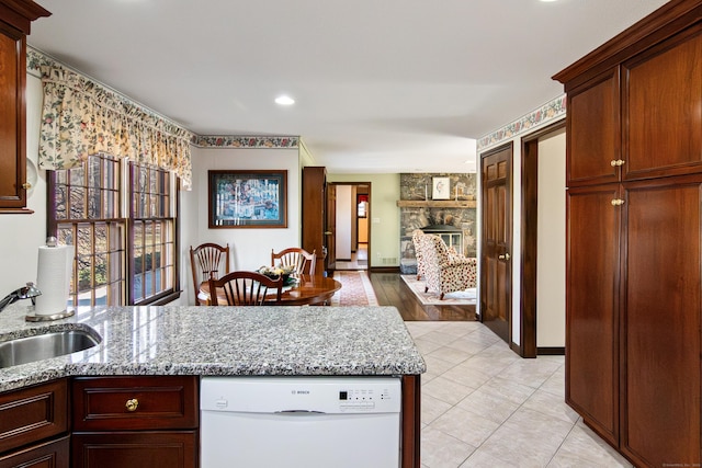 kitchen featuring light stone countertops, a stone fireplace, a peninsula, white dishwasher, and a sink