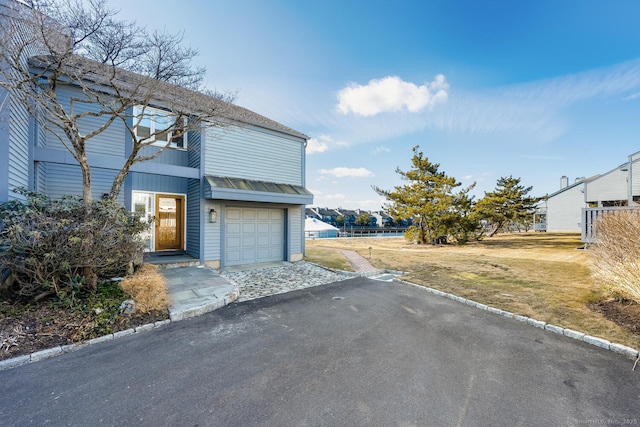 exterior space featuring a front yard, a standing seam roof, a garage, aphalt driveway, and metal roof