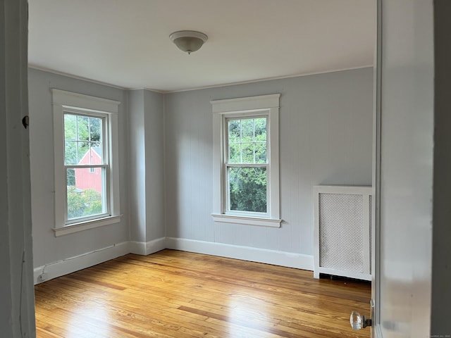 empty room featuring baseboards, light wood-style floors, and radiator heating unit