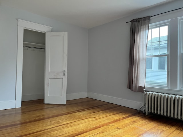 unfurnished bedroom featuring light wood finished floors, radiator, a closet, and baseboards