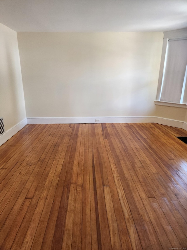 unfurnished room with baseboards, wood-type flooring, and visible vents