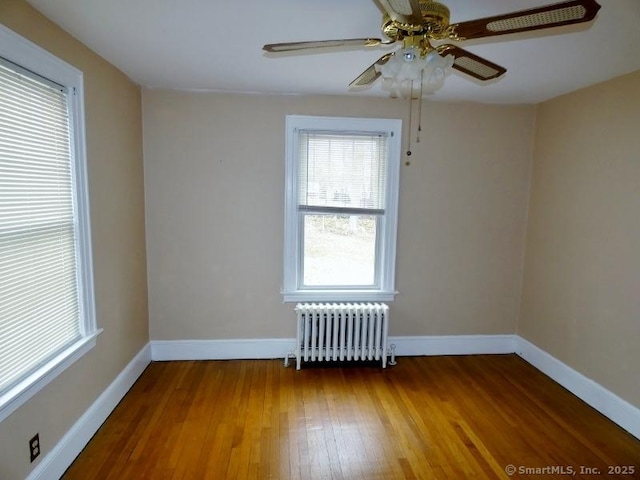 spare room with baseboards, radiator, a ceiling fan, and hardwood / wood-style flooring