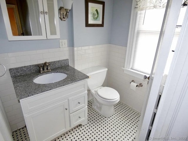 half bathroom featuring vanity, a wainscoted wall, tile patterned flooring, tile walls, and toilet