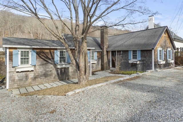 view of front of property with a chimney, gravel driveway, and a shingled roof