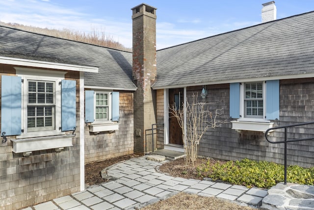 entrance to property with a chimney and roof with shingles