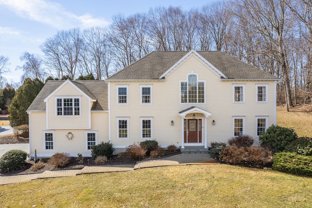 colonial inspired home with roof with shingles and a front yard