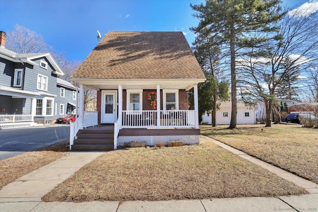 bungalow-style home with roof with shingles, a porch, and a front yard