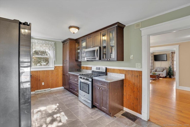 kitchen with a wainscoted wall, visible vents, wood walls, and stainless steel appliances