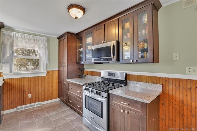 kitchen featuring a wainscoted wall, wooden walls, visible vents, and appliances with stainless steel finishes