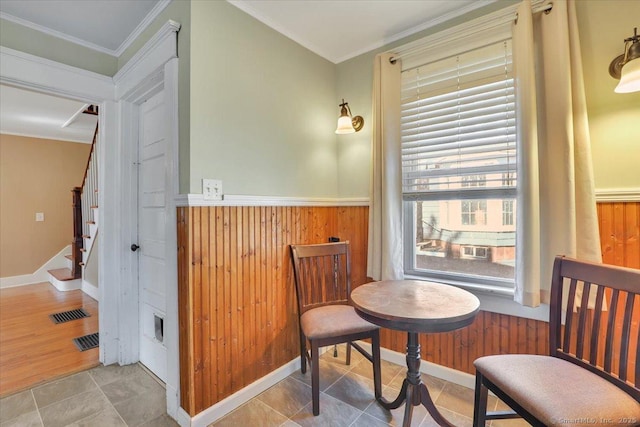 sitting room with stairway, wooden walls, visible vents, wainscoting, and crown molding