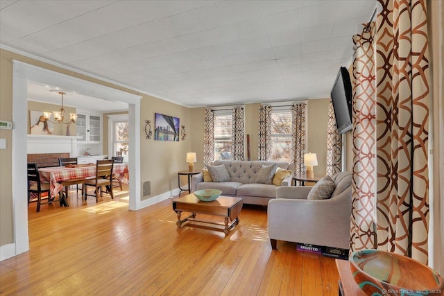 living room featuring visible vents, baseboards, an inviting chandelier, ornamental molding, and light wood-style floors