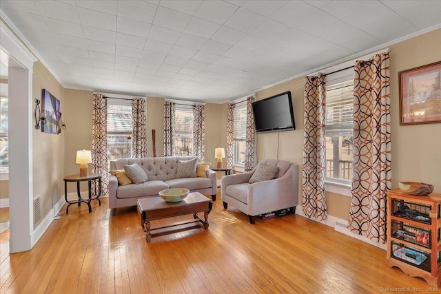 living room featuring visible vents, light wood-type flooring, baseboards, and ornamental molding