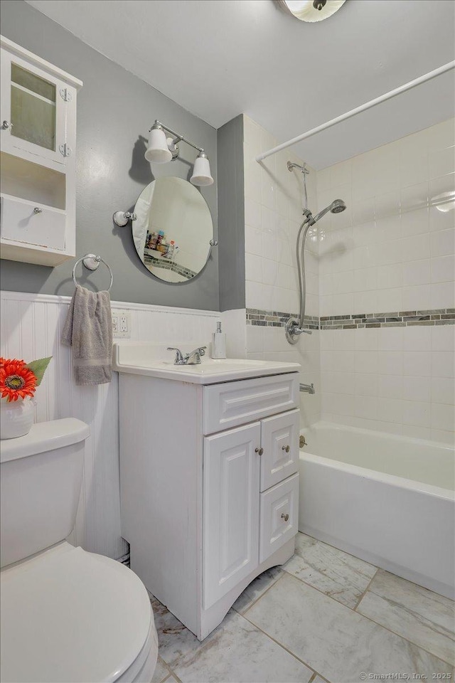 full bath with vanity, wainscoting, shower / tub combination, toilet, and marble finish floor