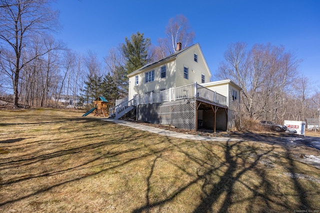 rear view of property featuring a wooden deck, a playground, a yard, and a chimney