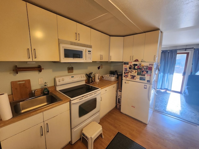 kitchen with white appliances, a textured ceiling, light wood-style floors, white cabinetry, and a sink