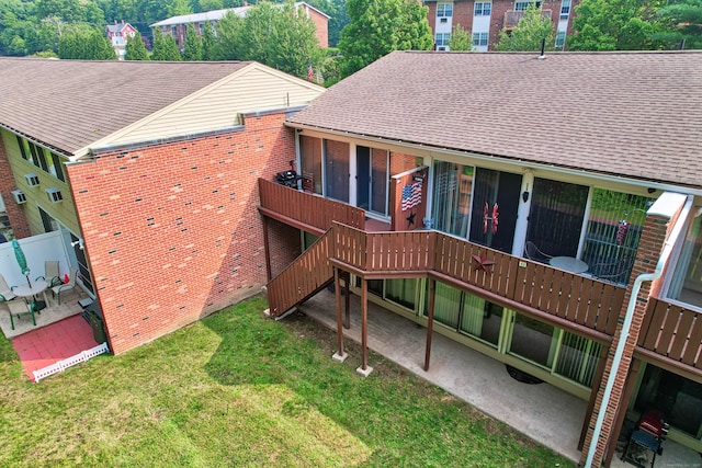 back of house with a patio, brick siding, roof with shingles, and a lawn